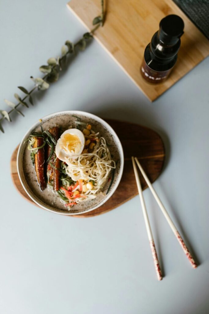 A flat lay of a vibrant ramen bowl with egg, vegetables, and chopsticks on a wooden plate.